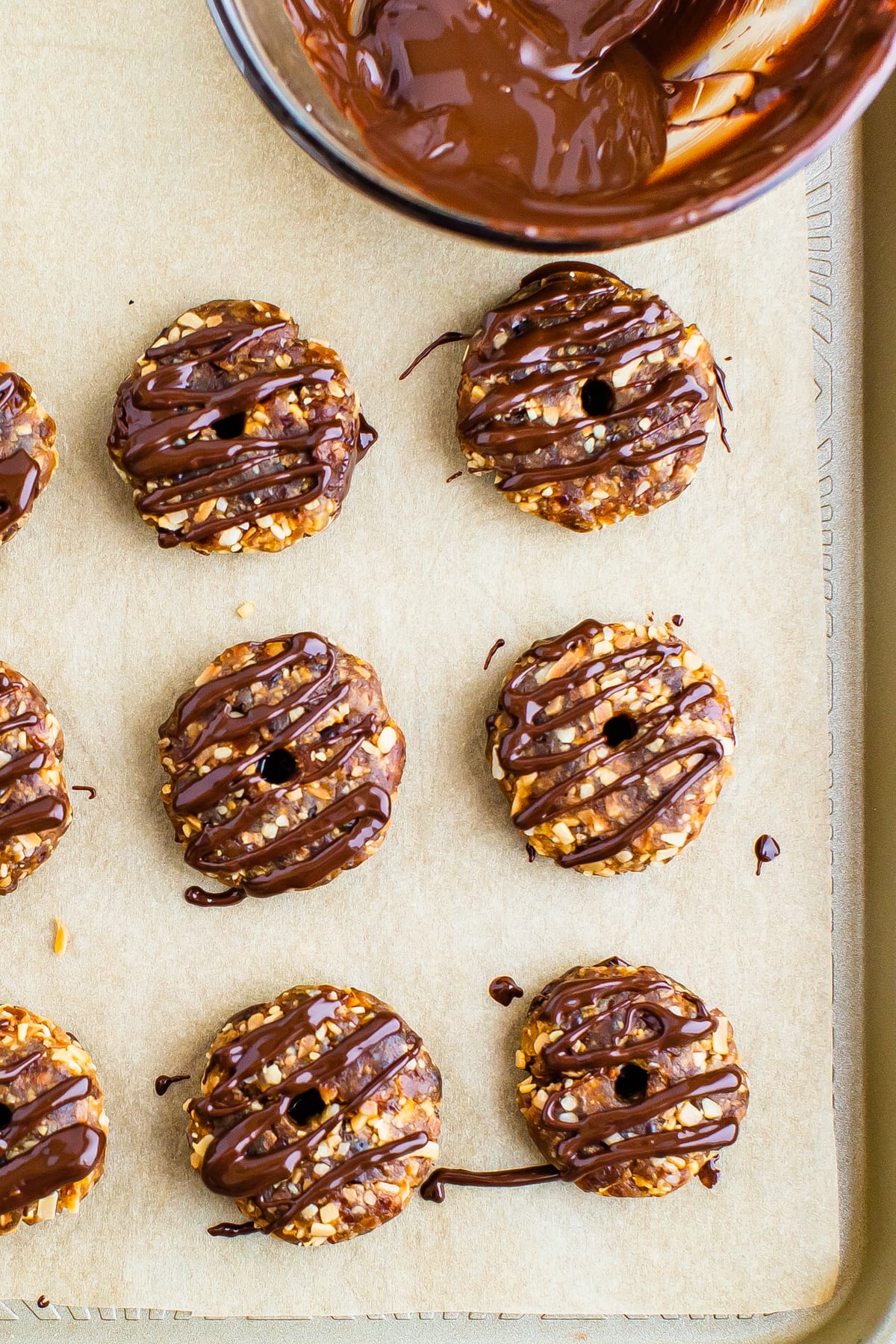 Parchment lined cookie sheet with homemade Samoas. A bowl of melted chocolate beside the cookies.