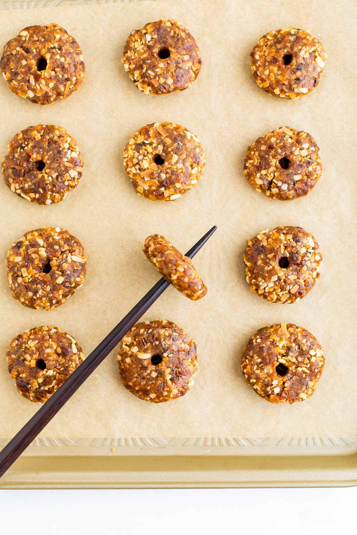 Donut shape no bake cookies on a parchment lined cookie sheet. A chop stick is making a hole in the middle of one of the cookies.