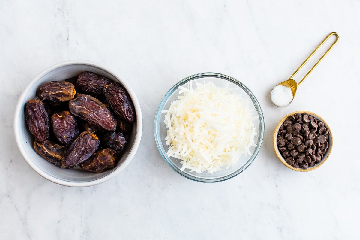 Three bowls of dates, coconut flakes and chocolate chips. Teaspoon of coconut oil.