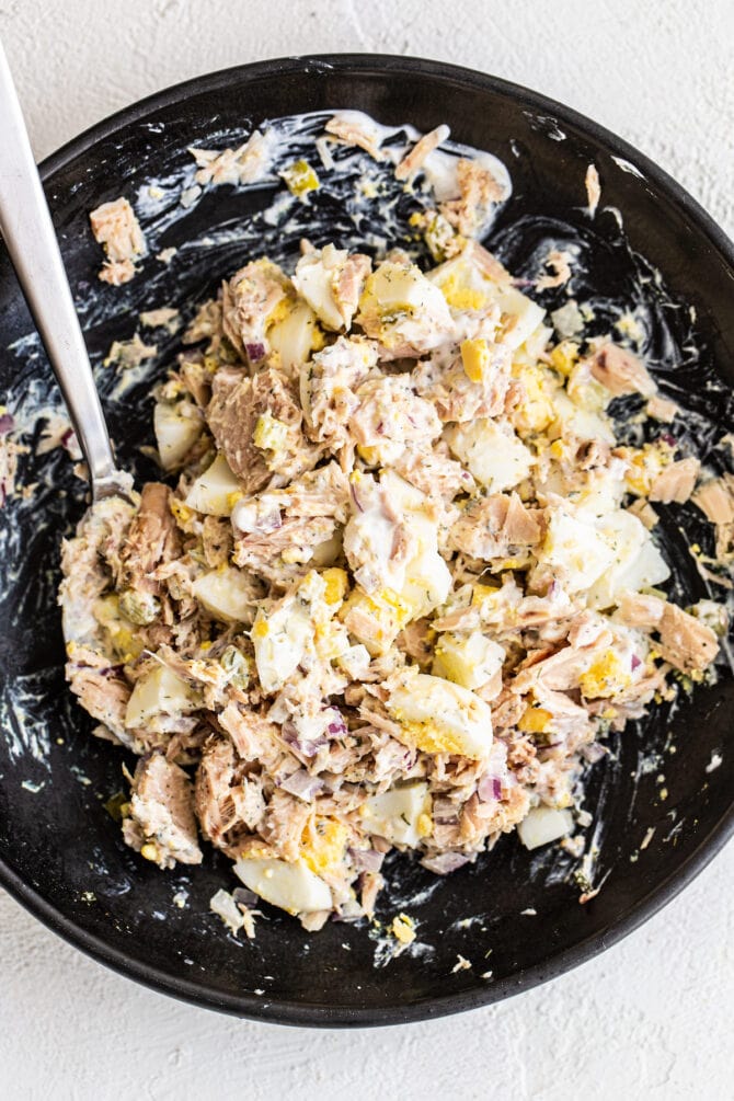 Bowl with a spoon mixing up tuna egg salad.