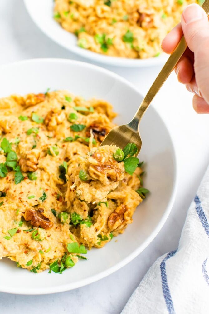 Fork taking a bite from a dish of spaghetti squash noddles with a creamy walnut sauce.