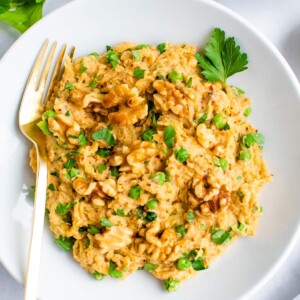 Plate of spaghetti squash noodles with a creamy walnut sauce and topped with walnuts and parsley.