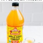 Bottle of apple cider vinegar and a measuring spoon next to a small bowl of apple cider vinegar.