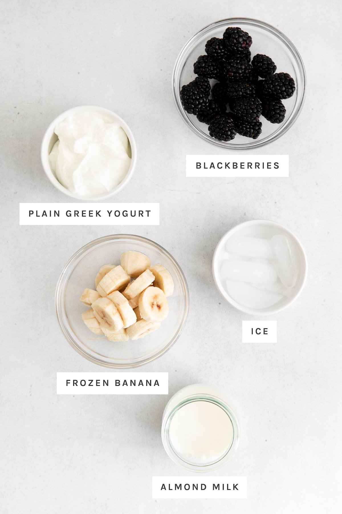 Measured out ingredients in bowls for blackberries, greek yogurt, ice, frozen banana and almond milk.