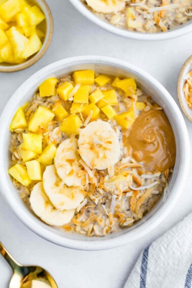 Bowl of overnight oats topped with pineapple, mango, coconut, banana and peanut butter.