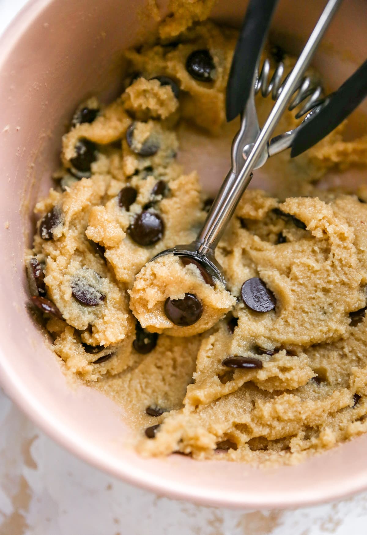 Mixing bowl of chocolate chip cookie dough with a cookie scoop.