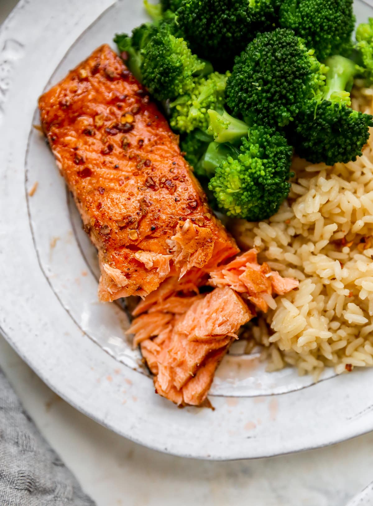 Plate with a piece of balsamic salmon, brown rice and broccoli. Salmon has a bite taken out of it.