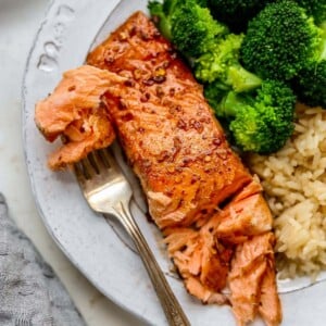 Plate with a piece of balsamic salmon, brown rice and broccoli. Fork is taking a bite from the salmon.