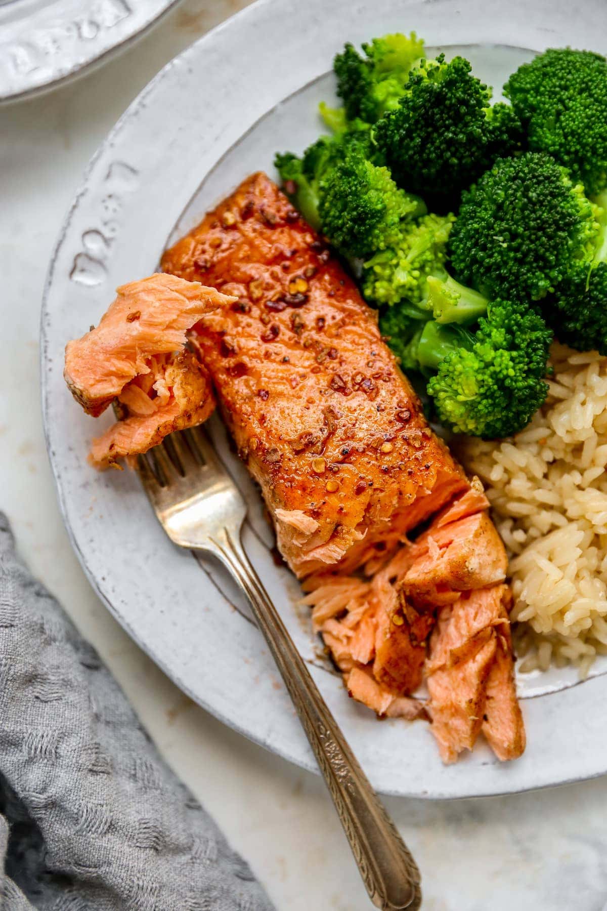 Plate with a piece of balsamic salmon, brown rice and broccoli. Fork is taking a bite from the salmon.