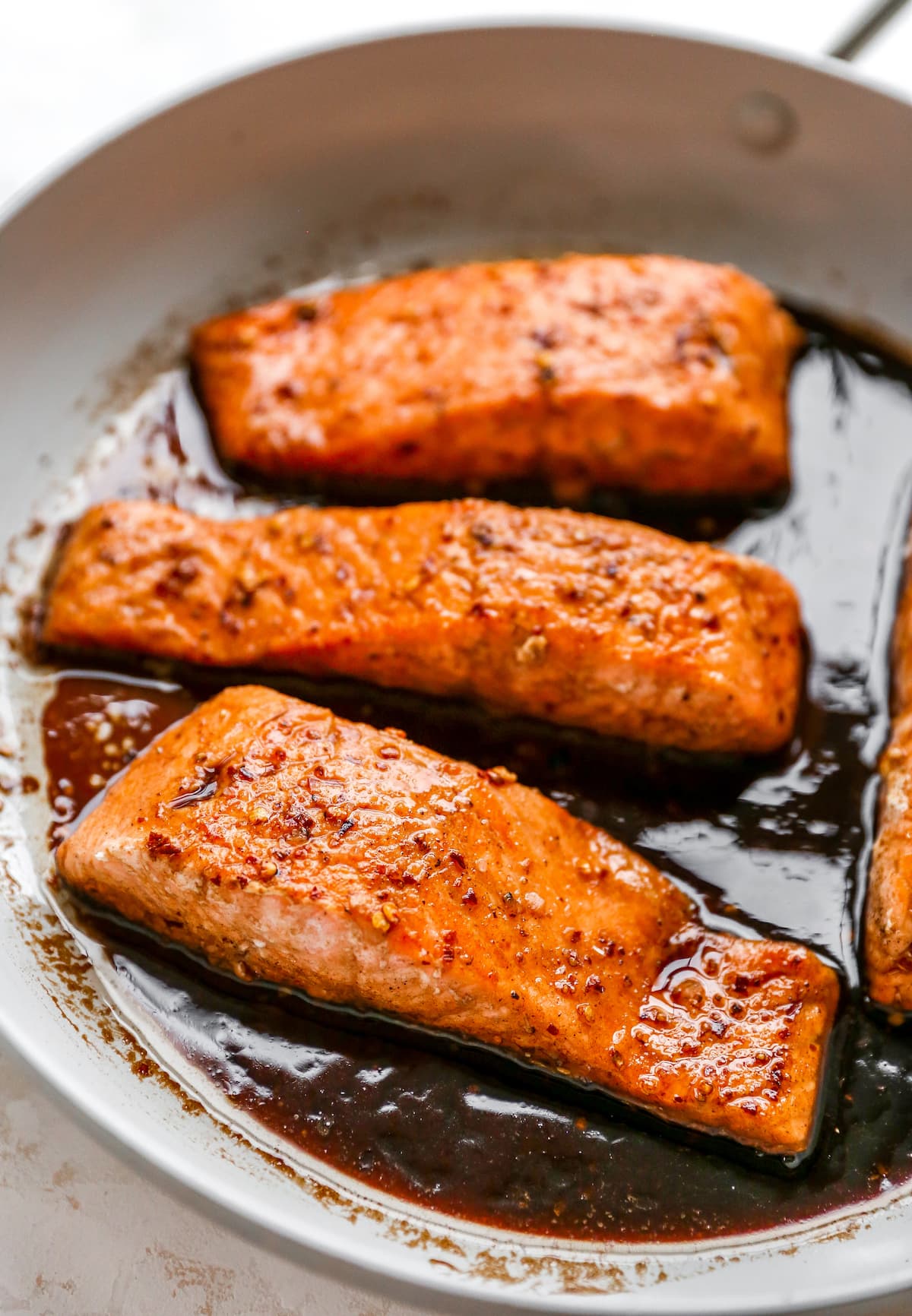 Four salmon filets in a skillet with balsamic glaze.