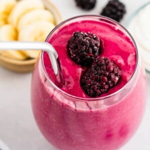 Glass of blackberry smoothie with a straw and blackberries on top.