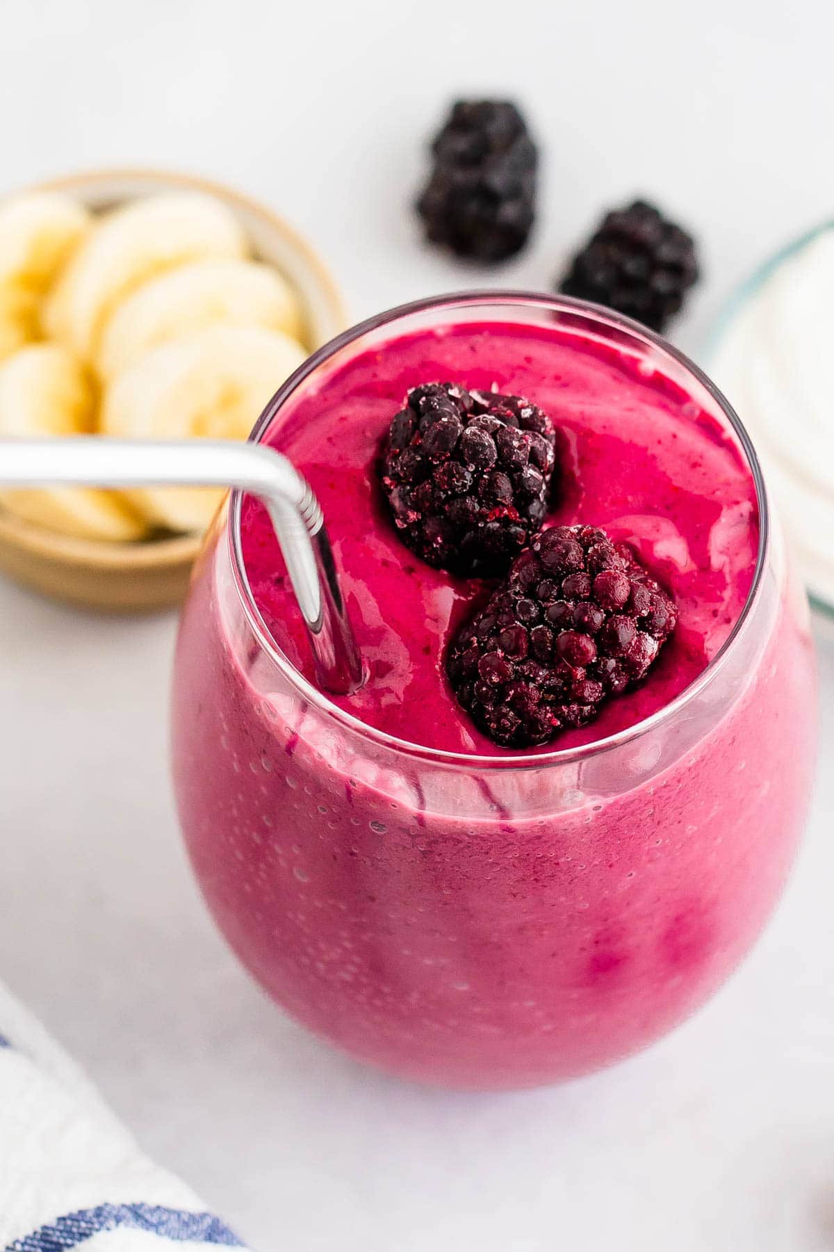 Glass of blackberry smoothie with a straw and blackberries on top.