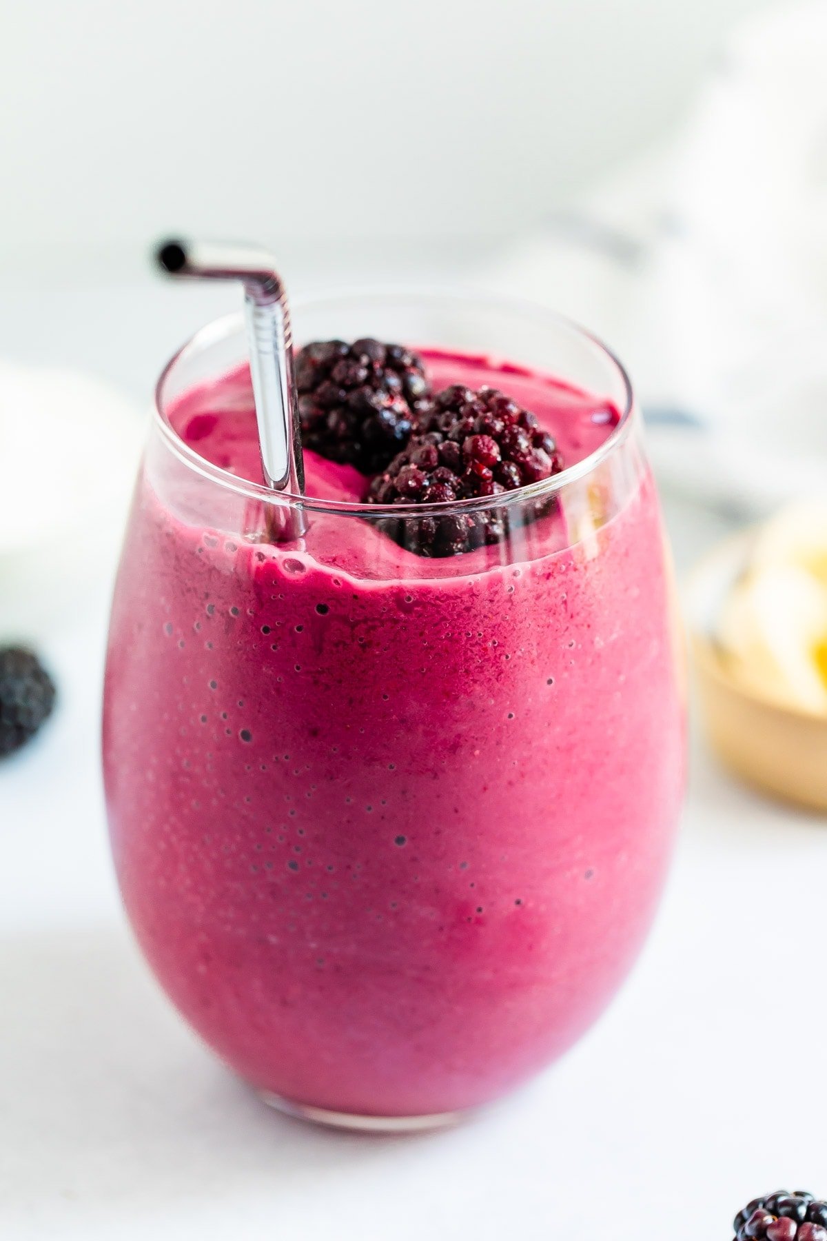 Glass of blackberry smoothie with a straw and blackberries on top.
