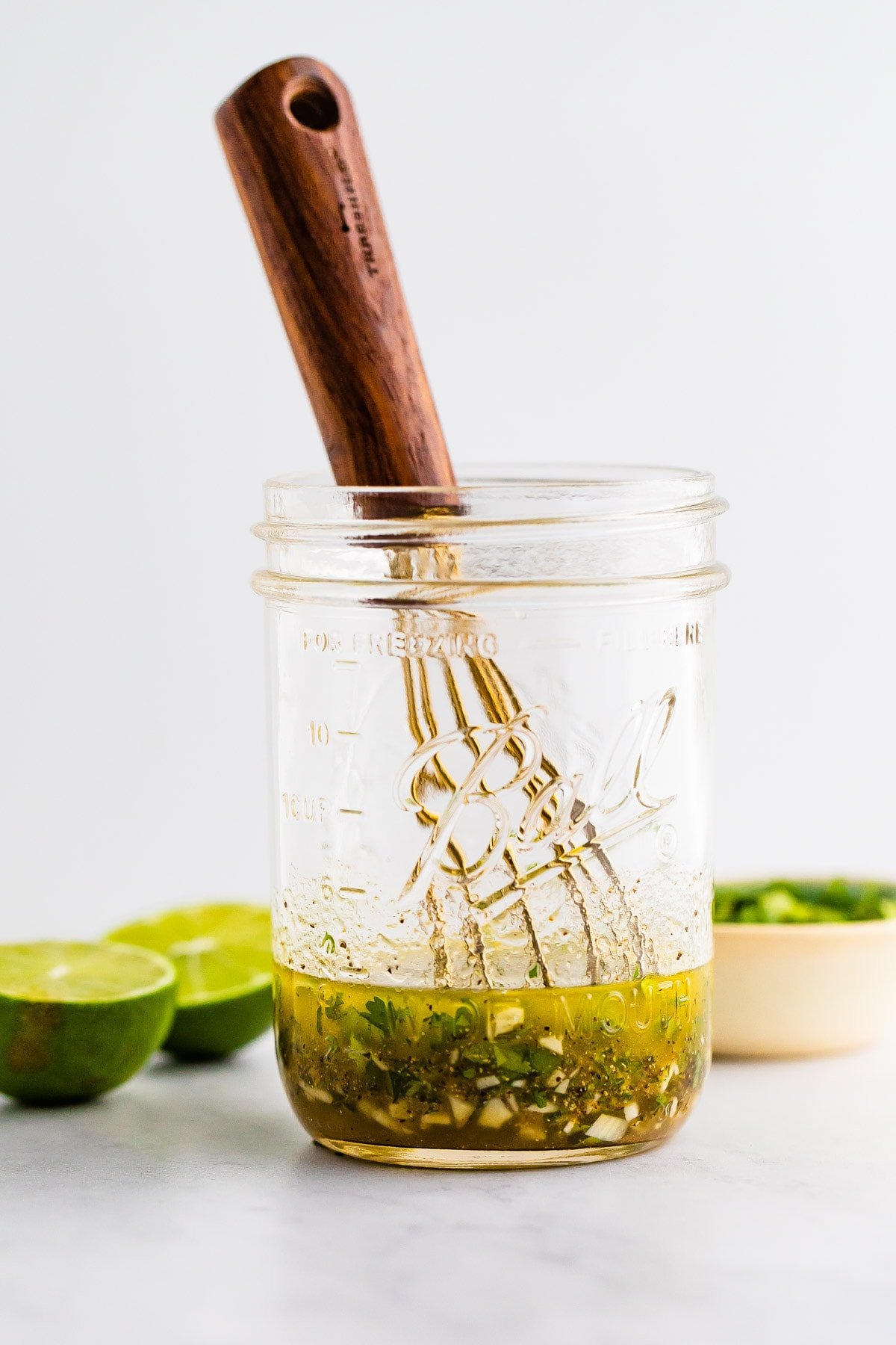 Mason jar with a whisk and ingredients for a cilantro lime dressing.