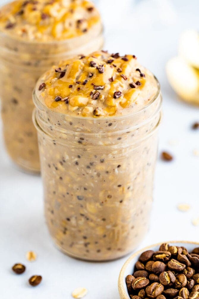 Two jars of coffee overnight oats topped with peanut butter and cocoa nibs.