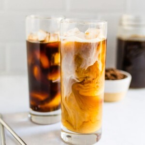 Two tall glasses of cold brew. One is black and one had cream being swirled in.