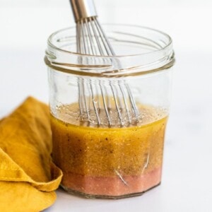 Jar of greek salad dressing with a little whisk.