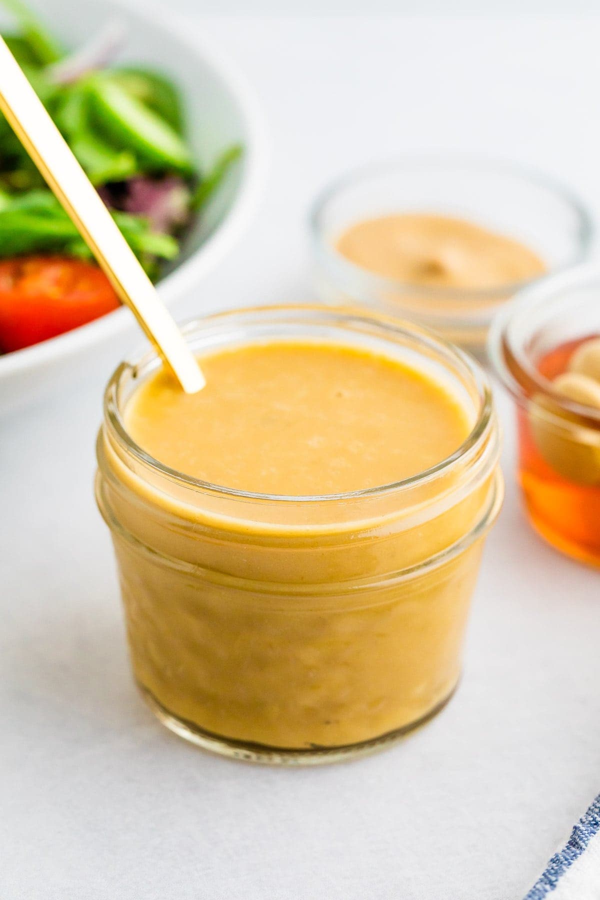 Jar and spoon with honey mustard dressing. A salad is behind the jar of dressing.
