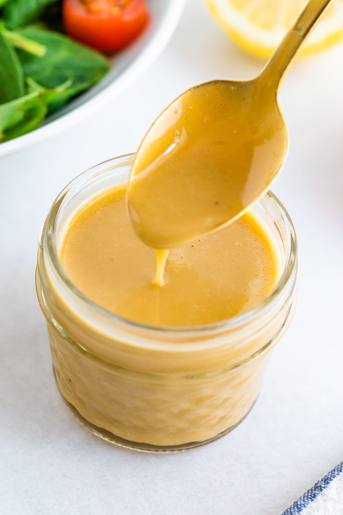Spoon drizzling some honey mustard dressing from a jar.