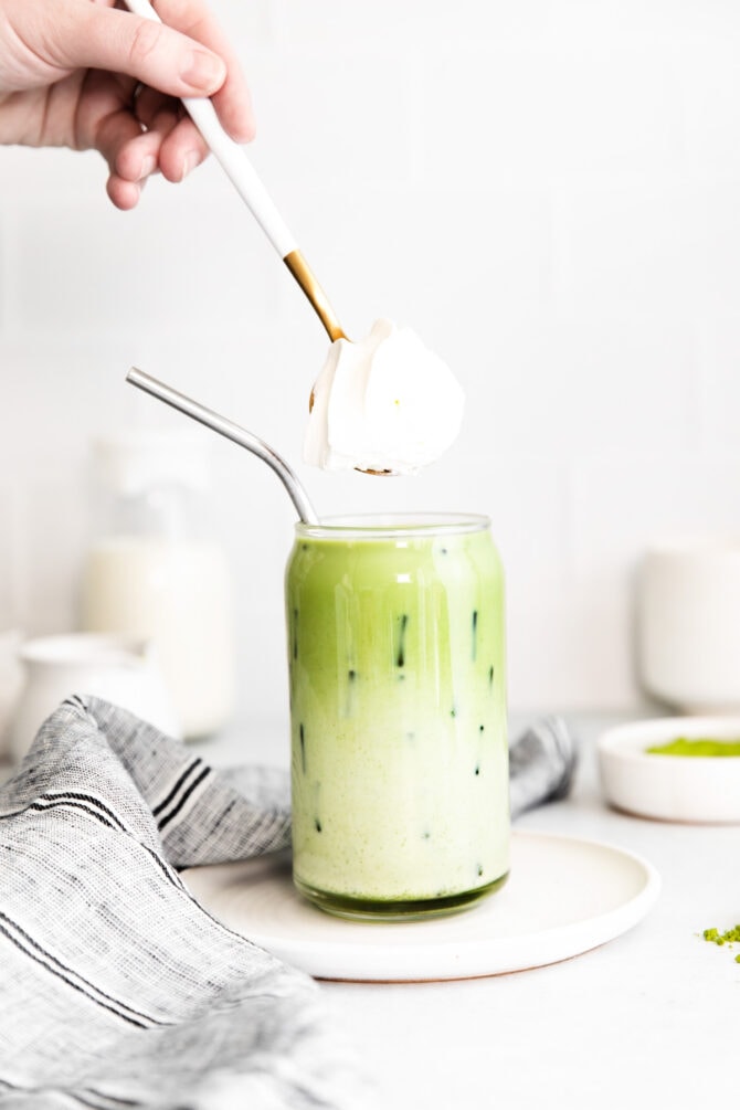 Topping iced matcha latte with whipped cream.
