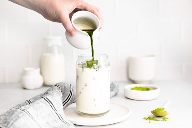 Pouring matcha into a glass of iced milk.