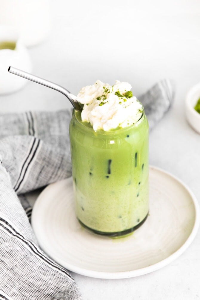 Iced matcha latte in a glass topped with whipped cream and a metal straw.