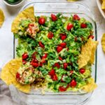Square dish of Mexican layer dip with tortilla chips in the dip.
