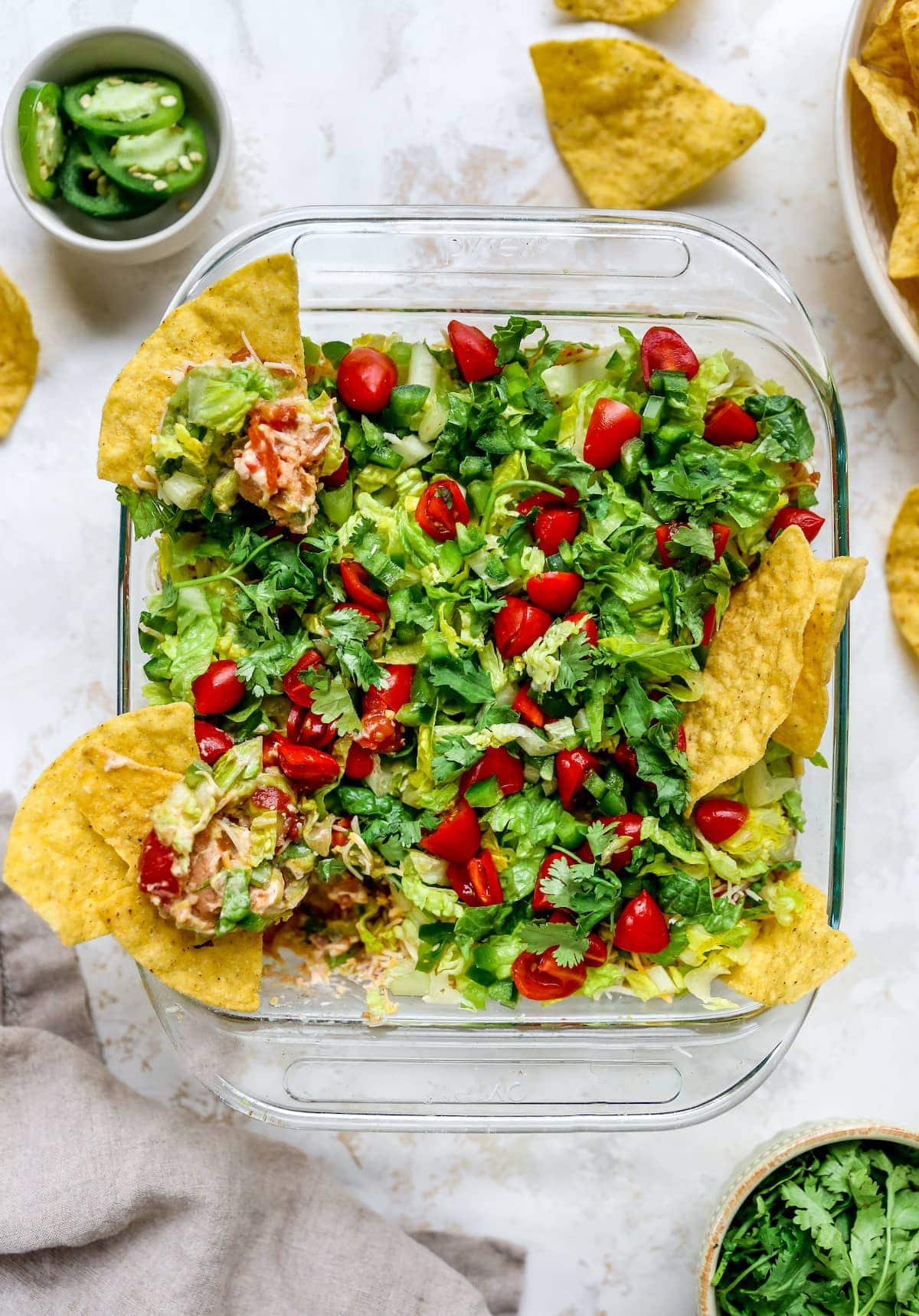 Square dish of Mexican layer dip with tortilla chips in the dip.