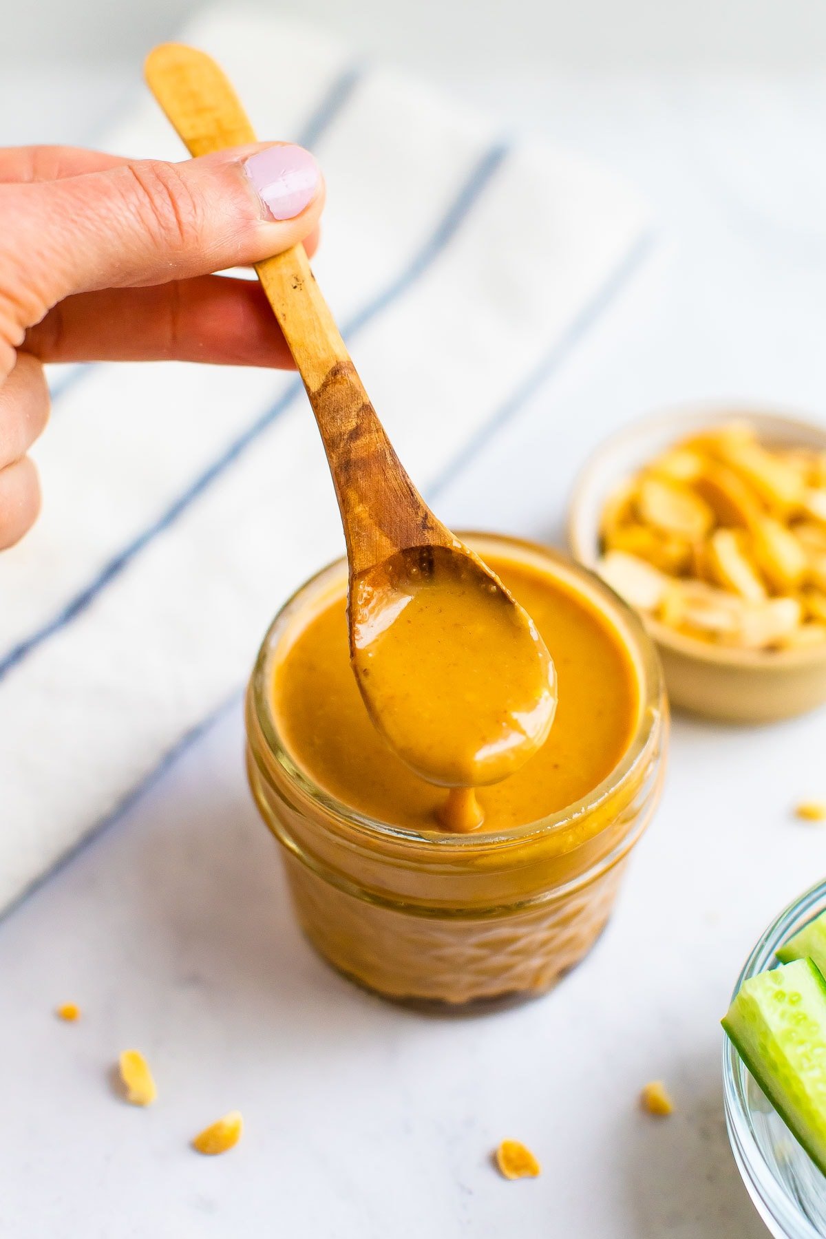 Spoon with a spoonful of peanut dressing from a small glass jar with peanut dressing.