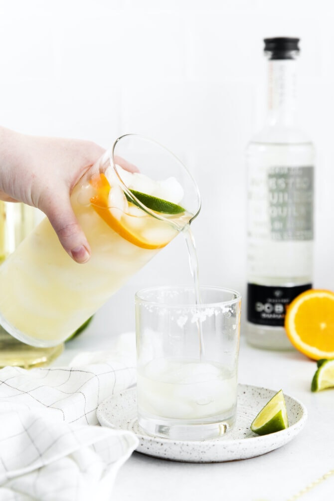 Pouring margarita mix into a glass of ice.