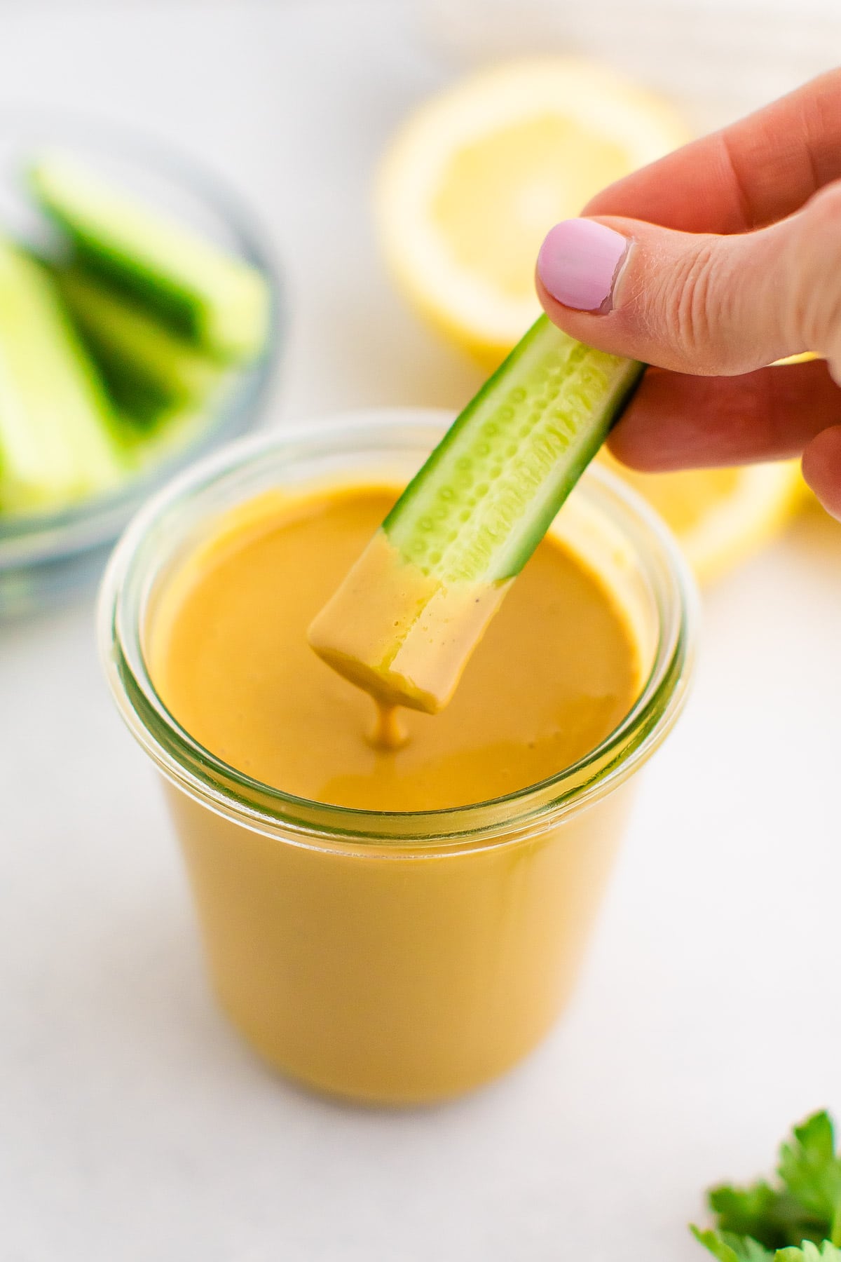 Person dipping a cucumber slice into a jar of tahini dip.
