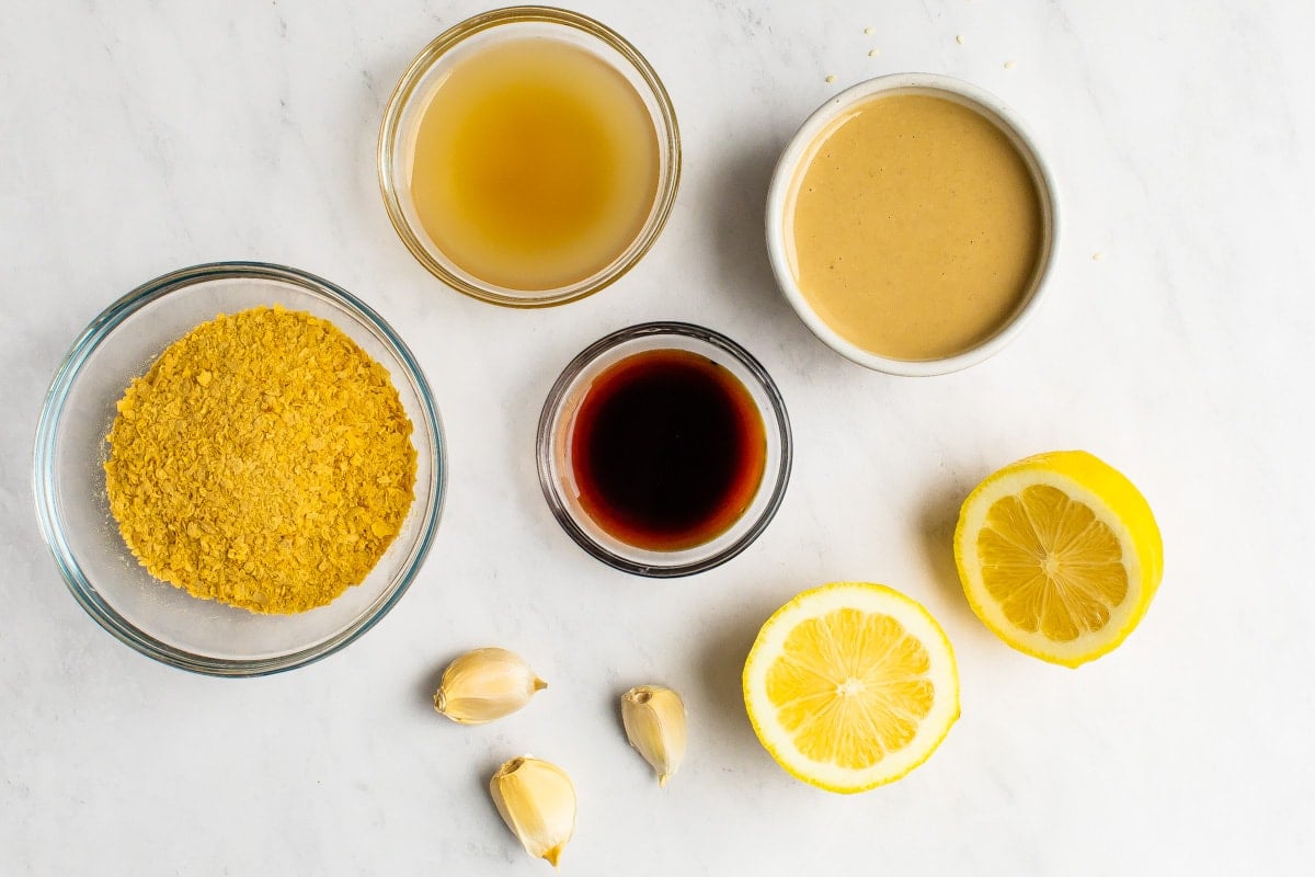 Tahini, lemon, nutritional yeast, vinegar, tamari and garlic measured out on a table.