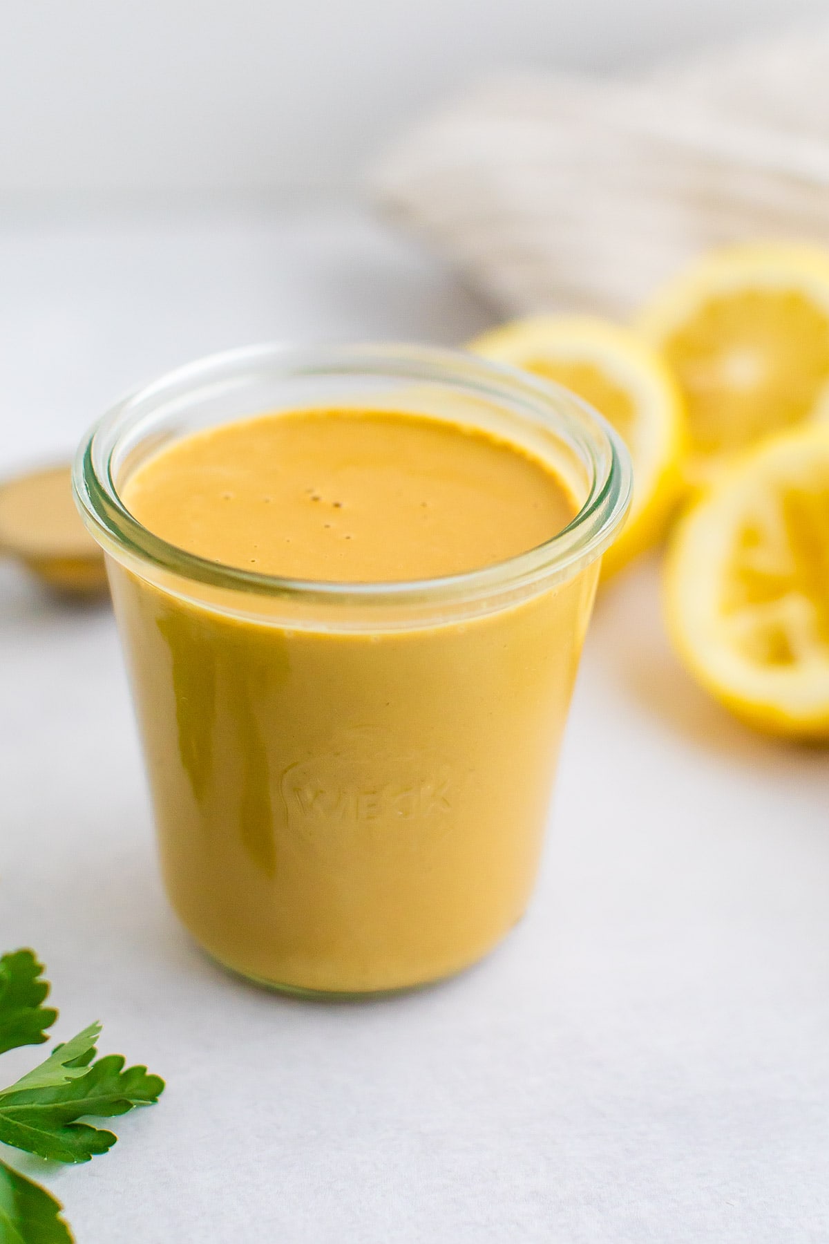 jar of homemade tahini dressing. Lemons and parsley are beside the jar.