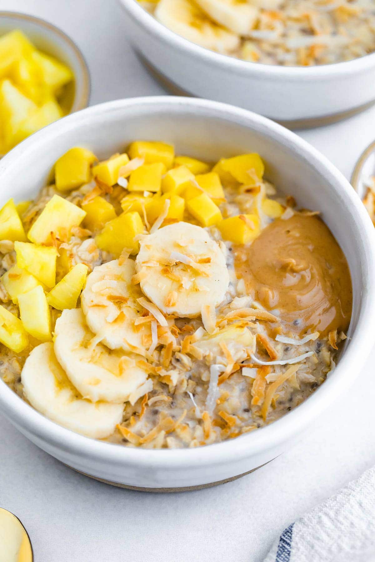 Bowl of overnight oats topped with pineapple, mango, coconut, banana and peanut butter.