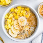 Bowl of overnight oats topped with pineapple, mango, coconut, banana and peanut butter.