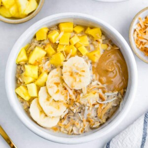 Bowl of overnight oats topped with pineapple, mango, coconut, banana and peanut butter.