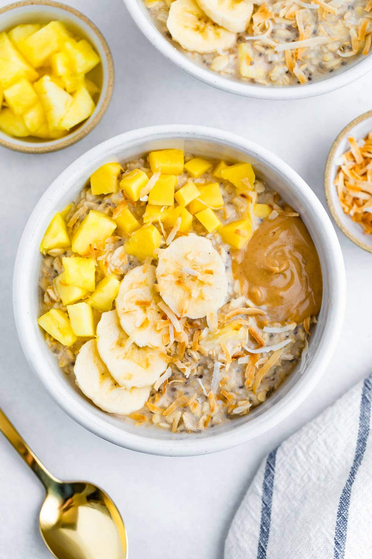 Bowl of overnight oats topped with pineapple, mango, coconut, banana and peanut butter.