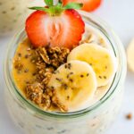Jar of overnight oats topped with banana, strawberries and granola and peanut butter.
