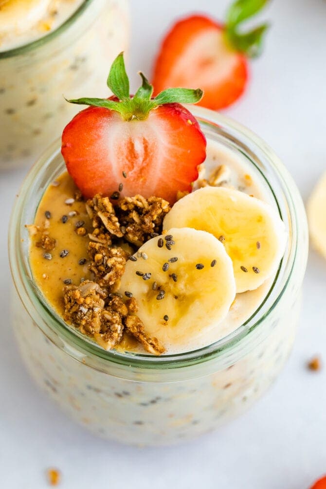 Jar of overnight oats topped with banana, strawberries and granola and peanut butter.