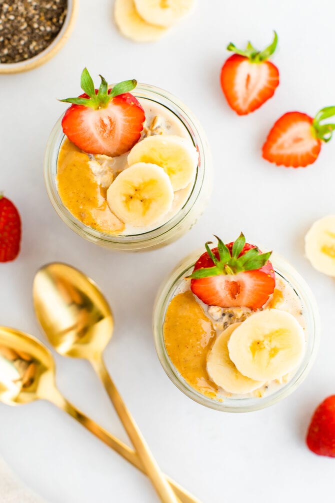 Two jars of overnight oats topped with peanut butter and fruit.