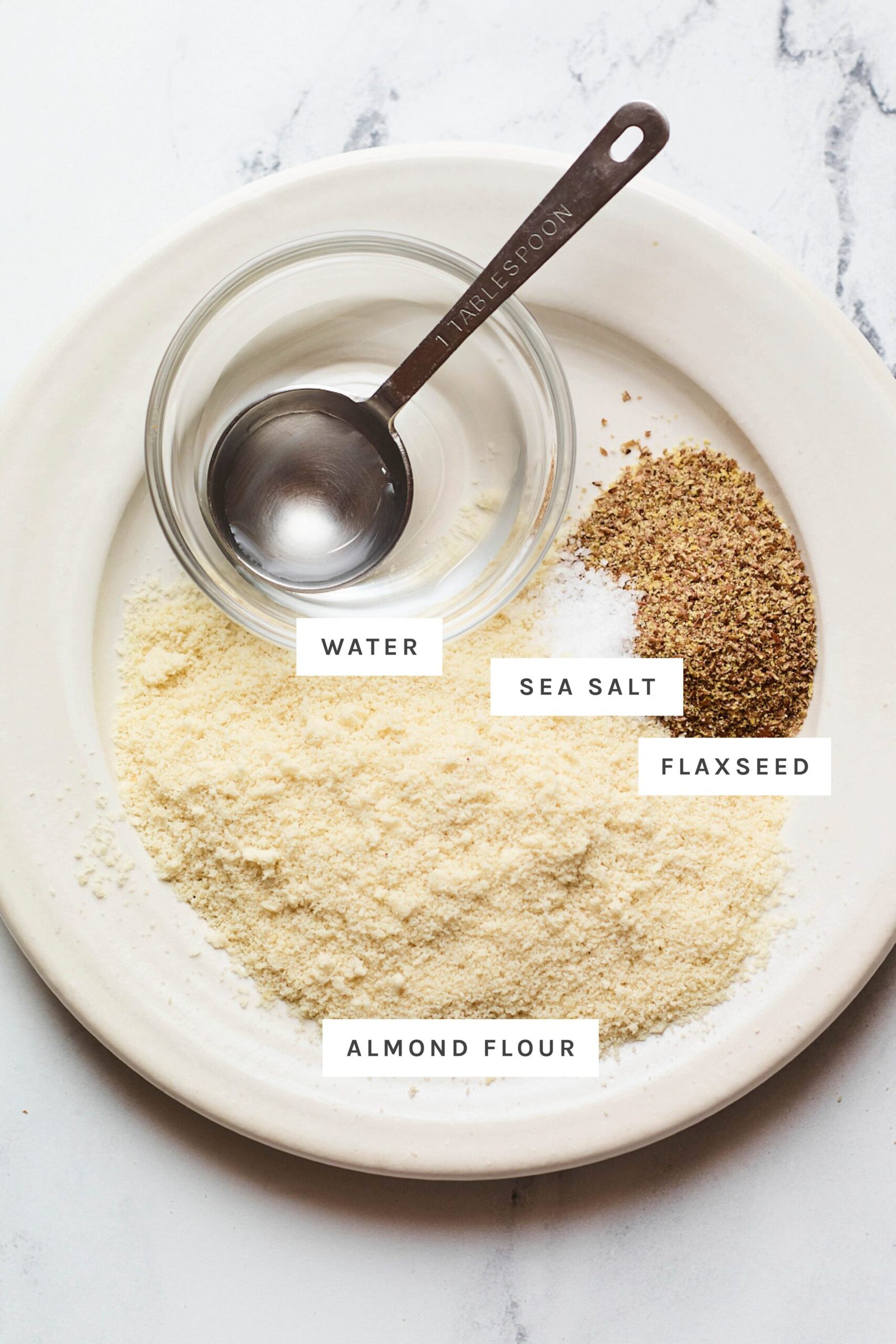 Water, flaxseed, salt and almond flour measured out on a plate.