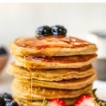 Stack of almond flour pancakes served with berries and maple syrup.