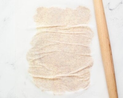 Rolling pin rolling out almond cracker dough between parchment paper.