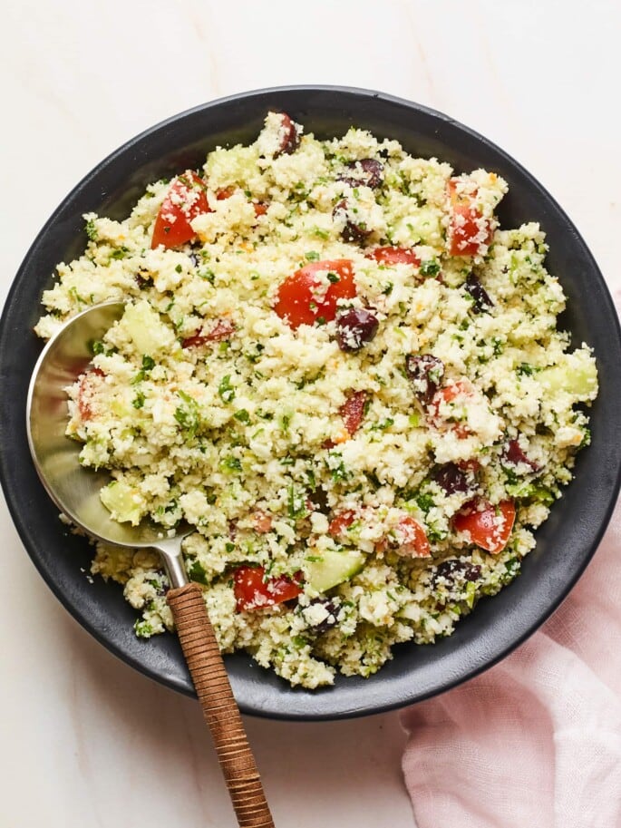 Serving bowl of cauliflower tabbouleh with a serving spoon.