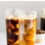 Two tall glassed of cold brew. One has a splash of milk swirling in the coffee.