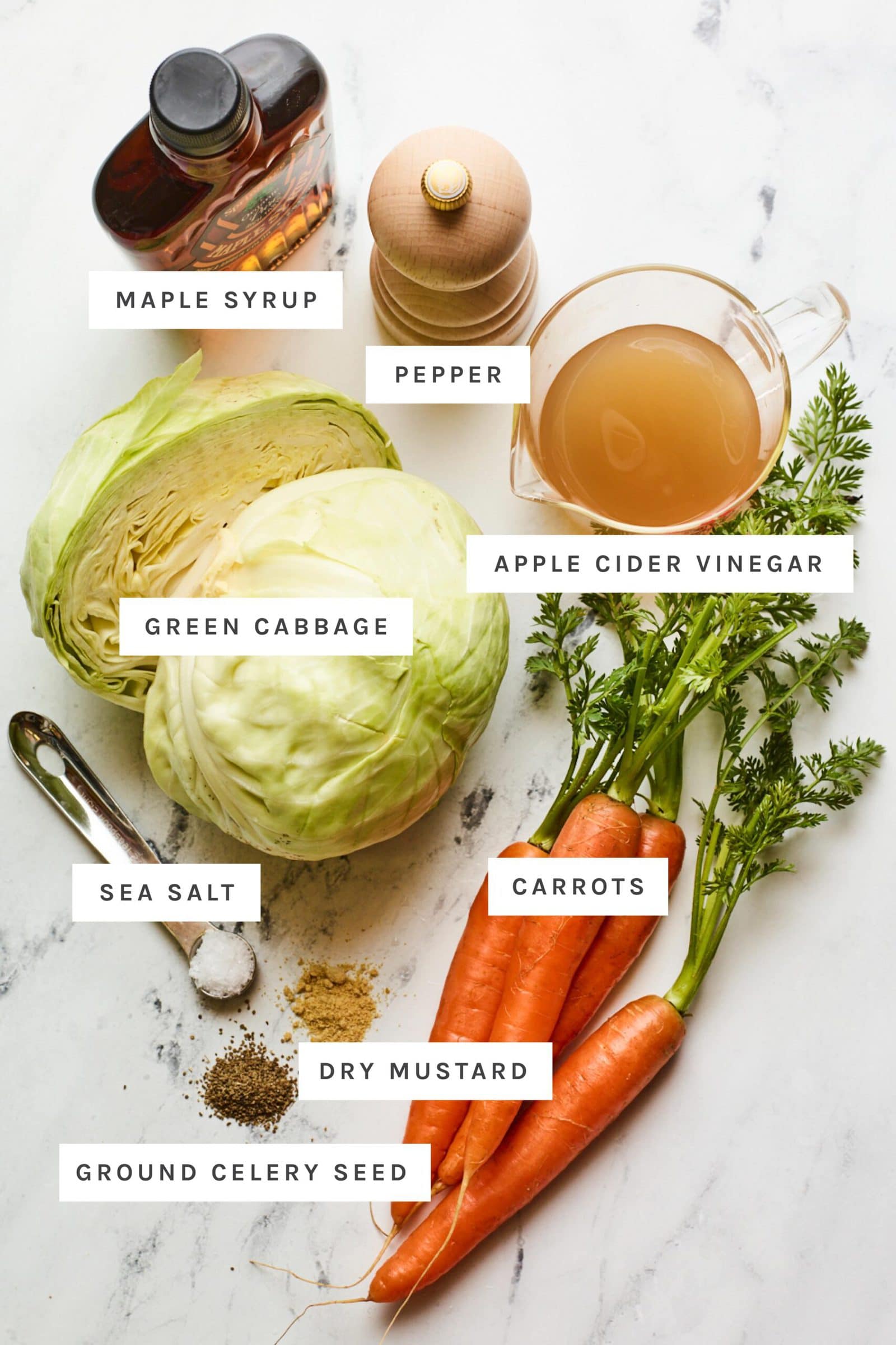 Ingredients to make apple cider vinegar coleslaw measured out on a table: cabbage, carrots, apple cider vinegar, maple syrup and spices.