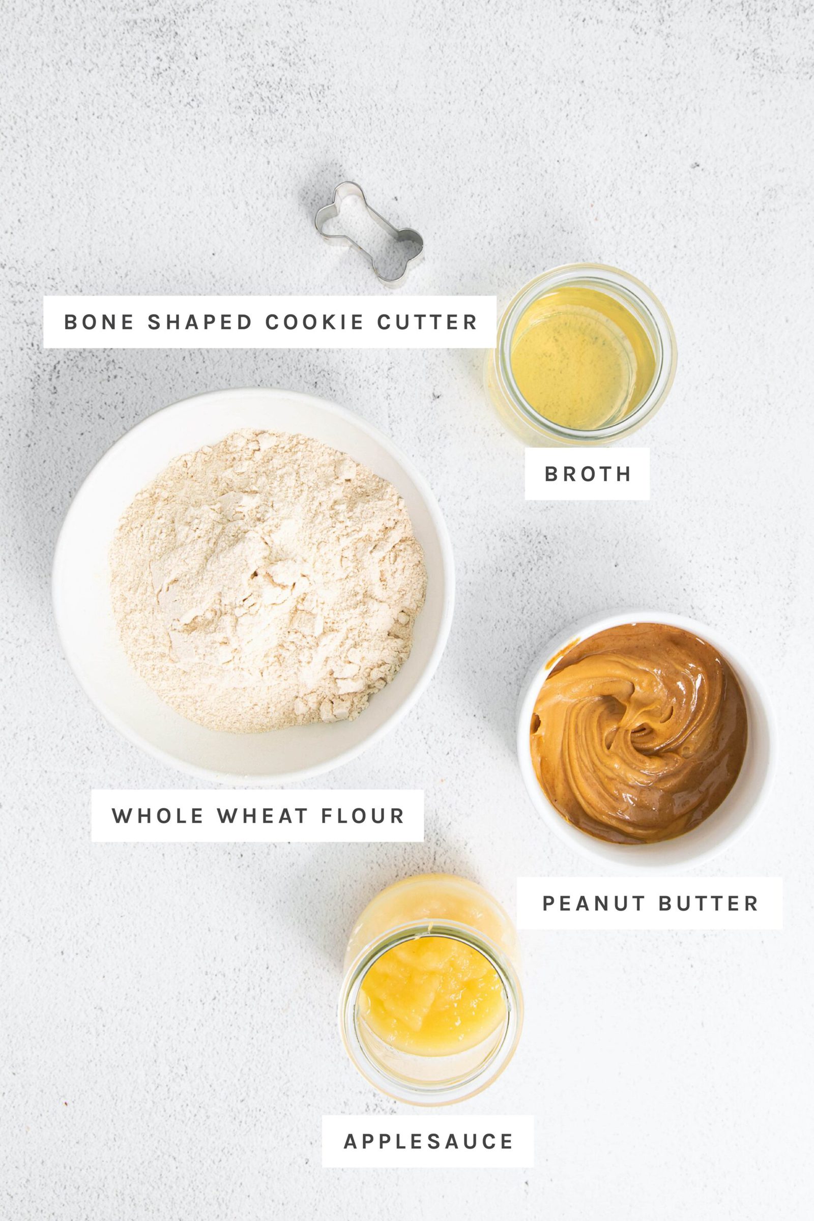 Cookie cutter, broth, wheat flour, peanut butter and applesauce measured out in bowls.