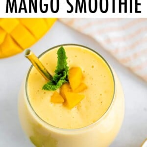 Mango smoothie in a glass with a metal straw and garnished with mint and mango chunks.