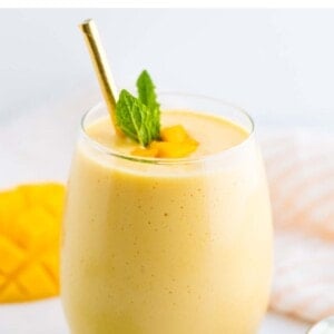 Mango smoothie in a glass with a metal straw and garnished with mint and mango chunks.