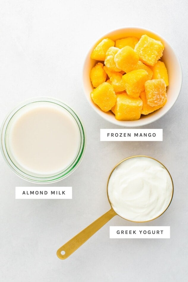 Frozen mango, almond milk and greek yogurt measured out in bowls and a measuring cup.